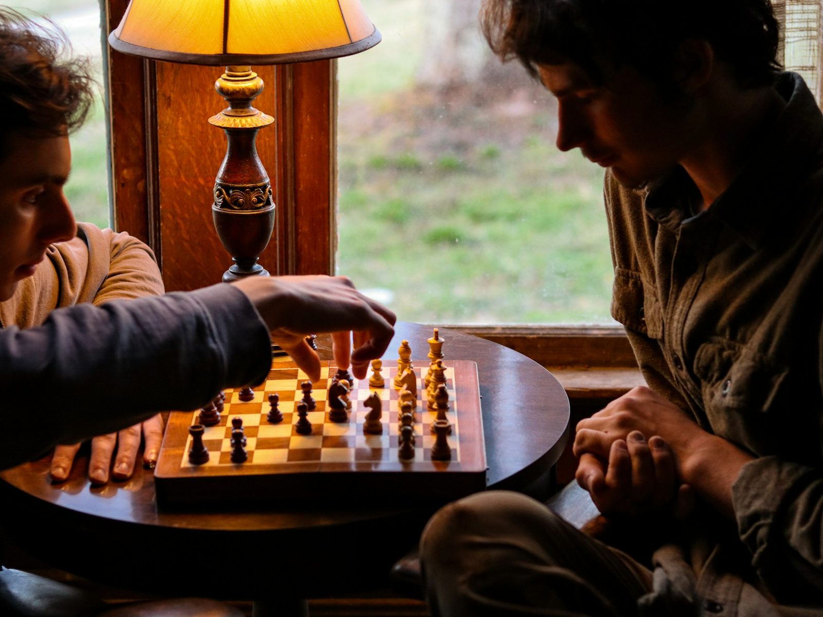 Two people playing chess at a table by a window